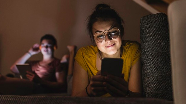 Mujer viendo su celular y su esposo al otro lado de la habitación viendo una tablet