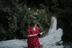 Mujer con vestido rojo sosteniendo una bilbia en la naturaleza