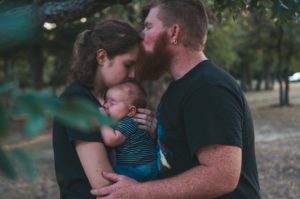 Padre besando a su esposa que abraza a su bebé en brazos
